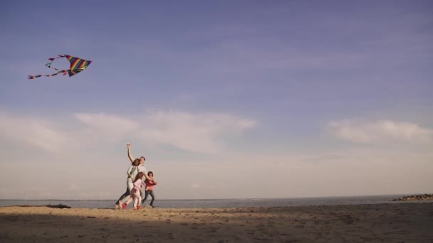 Família feliz lança um papagaio ao pôr-do-sol. início da primavera no mar. as crianças passam tempo com os pais ao ar livre. Pai, mãe e duas filhas num piquenique. câmara lenta — Vídeo de Stock