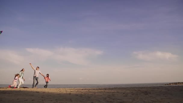 Lycklig familj lanserar en kite i solnedgången. tidigt på våren på havet. barn tillbringar tid med föräldrar utomhus. Far, mor och två döttrar på en picknick. slowmotion — Stockvideo