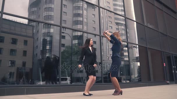 Две девушки в швейном бизнесе счастливы, прыгают и веселятся. деловая женщина празднует успех и победу. бизнесмены на фоне офисного здания из стекла. замедленное движение — стоковое видео
