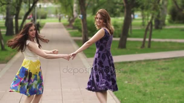 Привлекательные девушки прогуливаются по парку и улыбаются. Девушки проводят время вместе на открытом воздухе. девушки в ярких летних платьях прогуливаются в летнем парке. замедленное движение — стоковое видео