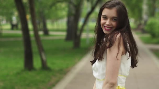 Retrato de jovem menina atraente com um belo sorriso. o modelo olha para a câmera e sorrindo. menina em um vestido de verão brilhante no Parque. câmara lenta — Vídeo de Stock