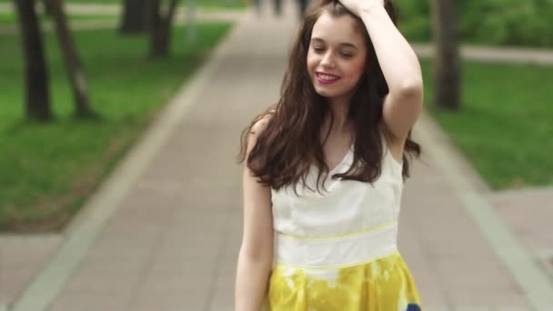 Portret młodego atrakcyjna dziewczyna z pięknym uśmiechem. model wygląda na aparat i uśmiechając się. Ubieramy dziewczynę w jasny lato w parku. zwolnionym tempie — Wideo stockowe
