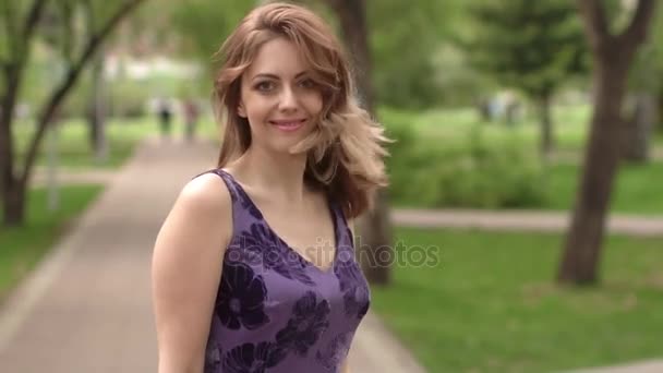 Porträtt av ung attraktiv flicka med ett vackert leende. modellen ser på kameran och leende. flicka i en ljusa sommar klänning i parken. slowmotion — Stockvideo