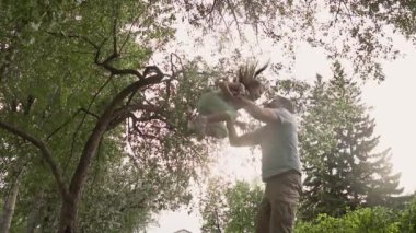 Baba küçük kızı havaya fırlatır ve onu yakalar. Baba çocukla çalış. küçük kız gülüyor ve gülümsüyor. Aile birlikte doğada vakit. Baba ve kızı sevgi ve hassasiyet.