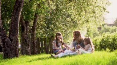 Anne ve iki kızı çimlere oturup elma ağaçlarının yakın. çocuklar ve anne gün batımında parkta. Anne ve kızı ihale ilişkisi.