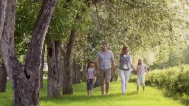 mutlu bir aile çiçek açması elma ağaçlarının yaz Parkı yürüme. Baba, anne ve iki kızı birlikte açık havada günbatımında vakit.