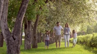 mutlu bir aile çiçek açması elma ağaçlarının yaz Parkı yürüme. Baba, anne ve iki kızı birlikte açık havada günbatımında vakit. Çocuklar ebeveynlerinin eller