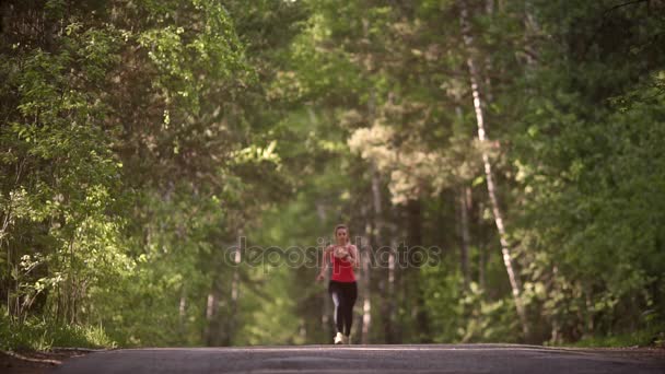 Giovane donna che fa jogging e si rallegra per il successo. la gioia e il gusto della vittoria dell'atleta. la ragazza attraente è impegnata in sport in una foresta estiva. rallentatore — Video Stock
