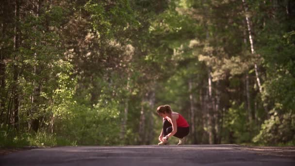 Jonge vrouw verbindt haar sneakers en bereidt zich voor op een jog. Een meisje met een slimme horloge doet sporten in de zomer bos. Slow motion — Stockvideo