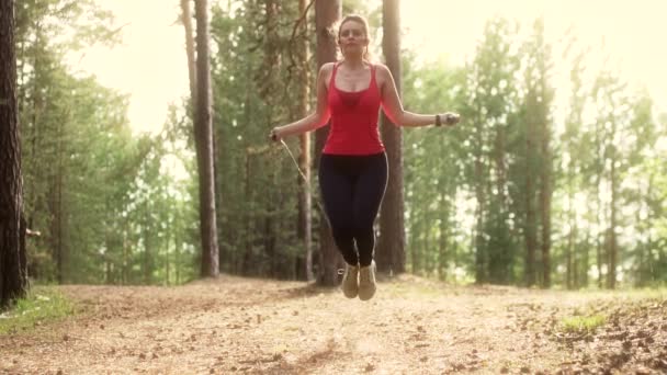 Chica entrena con una cuerda de saltar en un parque de verano en la puesta del sol. mujer joven haciendo deportes al aire libre. cámara lenta — Vídeos de Stock