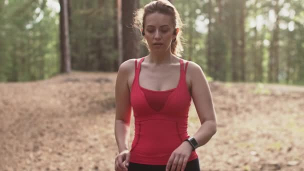 Mujer joven que se prepara para correr, comienza un seguimiento de entrenamiento en un reloj inteligente e incluye música en los auriculares inalámbricos. Movimiento lento — Vídeo de stock