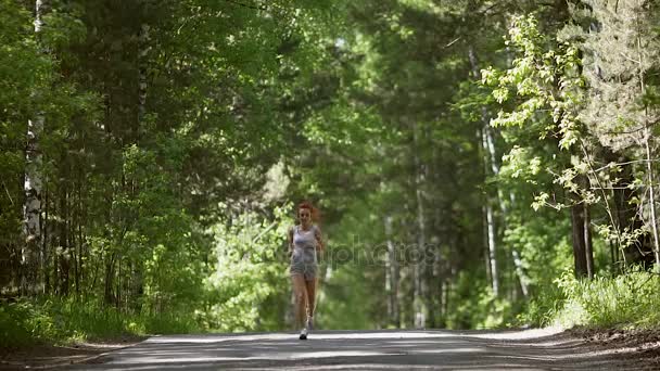 Молодая рыжая девушка бежит через лес. Красивая девушка занимается спортом и следит за здоровьем. замедленное движение — стоковое видео