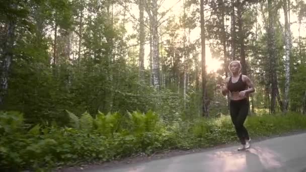 Chica musculosa en un ejercicio de carrera. Hermosa joven atleta dedicada a los deportes que corren en el bosque de verano. cámara lenta — Vídeo de stock