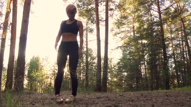 Atleta se prepara para o treinamento. Menina bonita fazendo alongamento ao pôr do sol na floresta — Vídeo de Stock