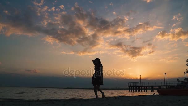 Porträtt av en attraktiv tjej gå barfota i sanden på stranden vid solnedgången. Silhuetten av en vacker flicka på stranden. slowmotion — Stockvideo