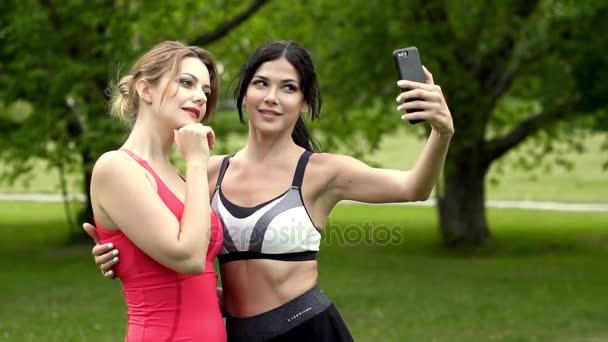 Dziewczyny czy selfie po joggingu. Dwie śliczne dziewczyny są fotografowane w przyrodzie na kamery telefonu komórkowego. zwolnionym tempie — Wideo stockowe