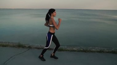 Plaj sahil boyunca günbatımında çalışan kız atlet. Kız günbatımında koşu