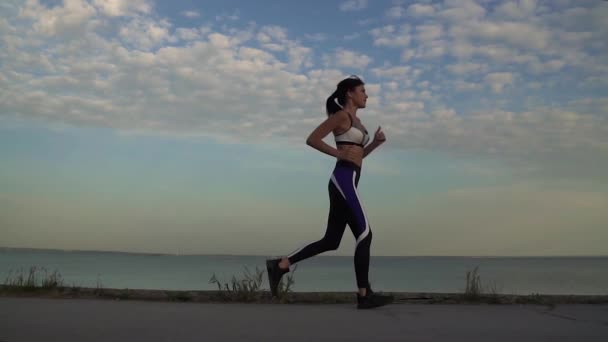 Fiatal nő fut finoman a surf-vonal mentén. A lány jogging, naplementekor — Stock videók