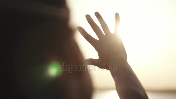 Dziewczyna patrzy na słońce przez jej rękę. dziewczyna jest w stanie spoczynku o zachodzie słońca. Womans ręka w słońcu. Machając ręką na słońcu — Wideo stockowe