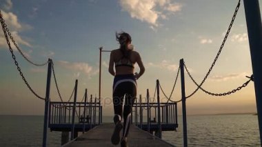 güzel bir rakam ile kız atlet deniz iskele üzerinde çalışır. sporcumuz çalışma tamamlandıktan ve mutlu bir şekilde ellerini yükseltir. genç bir kadın onu spor başarıları ve başarıları sahiptir