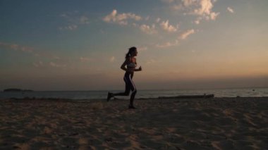 20'li yaşlarda batımında sahilde kum üzerinde çalışan kız. Açık havada yürüyüş. ağır çekim