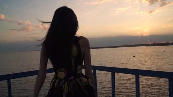 Silhouette eines schönen Mädchens in einem hellen Kleid bei Sonnenuntergang. ein Mädchen spaziert über einen Steg am Meer — Stockvideo