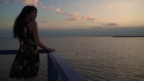 Silhouette eines schönen Mädchens in einem hellen Kleid bei Sonnenuntergang. Nahaufnahme Porträt eines Mädchens am Meer. ein Mädchen spaziert über einen Steg am Meer — Stockvideo