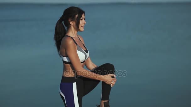 20s feminino desportivo aquece e começa a correr na orla. Menina atleta correndo ao longo da beira-mar na praia ao pôr do sol. A menina está correndo ao pôr do sol — Vídeo de Stock