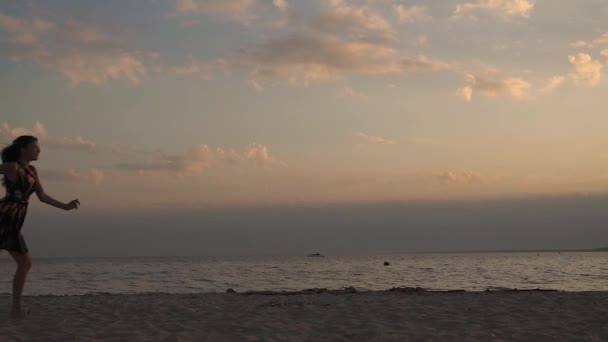 Menina bonita feliz correndo ao longo da praia e alegremente acenando seus braços. Jovem mulher ao pôr do sol na praia — Vídeo de Stock