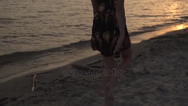 Hermosa chica en vestido ligero caminando en la playa al atardecer y sonriendo — Vídeo de stock