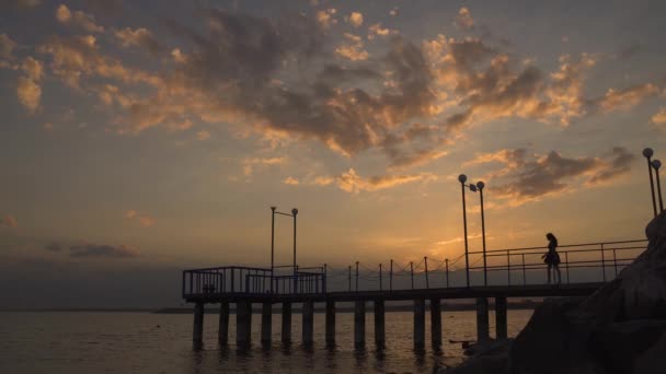 Silhouet van een mooi meisje lopen op een pier bij zonsondergang — Stockvideo