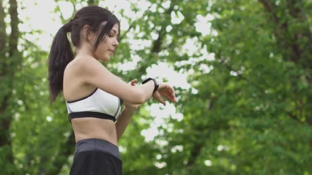 Chica de deportes ejecuta un programa de entrenamiento en reloj inteligente y empezar a correr. Mujer joven haciendo deportes en la naturaleza . — Vídeo de stock