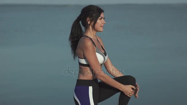 20s sportig kvinna värms upp och börjar köras vid vattnet. Flicka-idrottsman nen kör längs havet på stranden vid solnedgången. Flickan jogging i solnedgången — Stockvideo