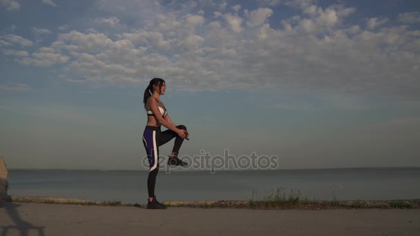 20 代スポーティな女性を温め、ウォーター フロントに実行を開始します。夕暮れ時のビーチの海岸に沿って実行している女の子の選手。夕暮れ時、女の子をジョギングします。 — ストック動画