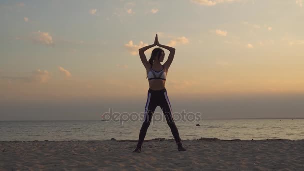 Όμορφη νεαρή γυναίκα σε αθλητικά ρούχα γιόγκα σε εξωτερικούς χώρους. 20s κορίτσι κάνει ασκήσεις αναπνοής ξημερώματα στην παραλία... αργή κίνηση — Αρχείο Βίντεο