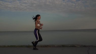 genç kadın hafifçe sörf hat boyunca çalışır. Kız günbatımında koşu