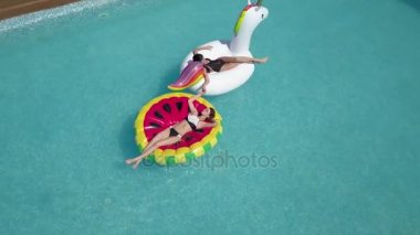 Anteni - döşeme ve yakınındaki rahat 20s, yaz tatili havuzu genç seksi bayanlar. Bir tek boynuzlu at ve karpuz şeklinde şişme yatak güneşlenme yatan kız vardır.