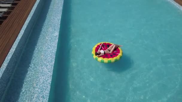 Aerial - jovem mulher sexy relaxante no colchão de melancia inflável na piscina de água cristalina. A rapariga toma banho de sol na praia. Tiro do ar com quadricóptero — Vídeo de Stock