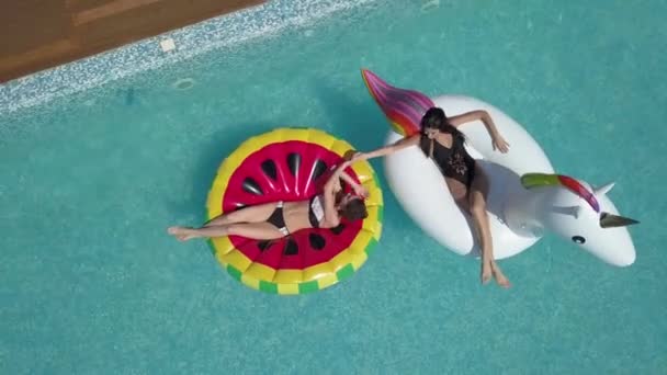 Aérea - Jóvenes hermosas novias están tomando el sol en la piscina acostados en colchones inflables. Chicas jóvenes y atractivas descansan en un día soleado. Tiro con quadrocopter — Vídeo de stock