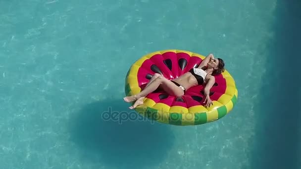 Antenne - sexy Mädchen im Badeanzug, die sich auf einer aufblasbaren Matratze in Form einer Wassermelone sonnt. Brünette Sonnenbräune im Pool. Schießen mit Quadrocopter — Stockvideo