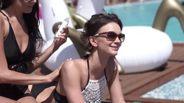 Flicka i en bikini sätter en solskyddsfaktor på ryggen vänner. Vackra flickor sola och ha kul vid poolen. slowmotion — Stockvideo