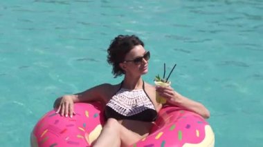 Mayolu şişme bir şilte üzerinde bir tek boynuzlu at yalan güneşlenme içinde genç bir kadın. Çekici kız bikinili ferahlatıcı bir kokteyl sahiptir ve havuzda yüzüyor