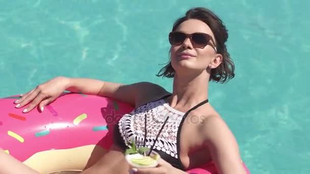 Ritratto di una ragazza in bikini che prende il sole su un materasso gonfiabile in piscina. Bella giovane donna bere un cocktail e godersi una calda giornata di sole — Video Stock