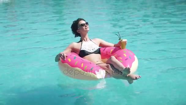 Hermosa chica en gafas de sol tomando el sol tumbado en un colchón inflable donut. Mujer joven disfruta de relajarse y se baña en la piscina al aire libre — Vídeos de Stock