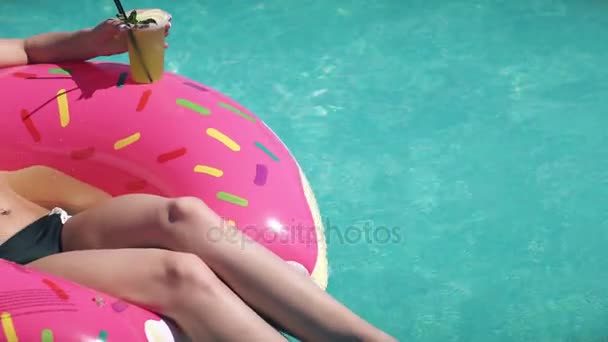 Nahaufnahme einer jungen Frau im Bikini. schöne Mädchen mit Sonnenbrille trinkt ein Erfrischungsgetränk, das auf einem aufblasbaren Matratzen-Donut in einem Außenpool liegt — Stockvideo