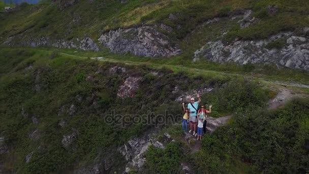 Aéreo. feliz família de viajantes sentados à beira do penhasco, balançando os braços e sorrindo para a câmera. pai e mãe com suas filhas ao ar livre ao pé das falésias . — Vídeo de Stock