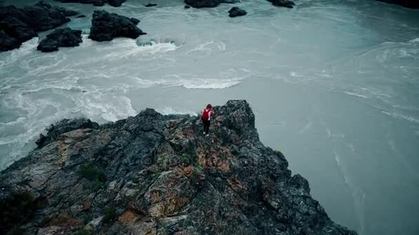 Aereo. viaggiatore ragazza con zaino sul bordo di una scogliera in un fiume di montagna. giovane donna godendo di una vista mozzafiato. Altai, Siberia. Fotocamera aerea ripresa — Video Stock