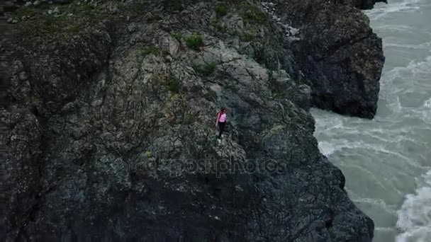 Antenowe. Kobieta dla podróżujących z plecakiem korzystających wspaniały stały widok na skraju urwiska na górskiej rzece. Ałtaj, Siberia. Aerial strzał kamera — Wideo stockowe