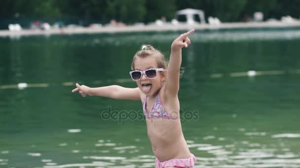 Niña tonteando y haciendo caras graciosas. el niño bañándose en el lago y disfruta de un día caluroso de verano. Movimiento lento — Vídeo de stock