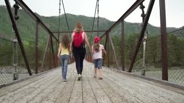 Anne ve kızı yağmur Bridge'de boyunca yürüyor. Aile dağlarda yayılıyor. Genç kadın turist çocuk ile yürüyen bir sırt çantası ile. ağır çekim
